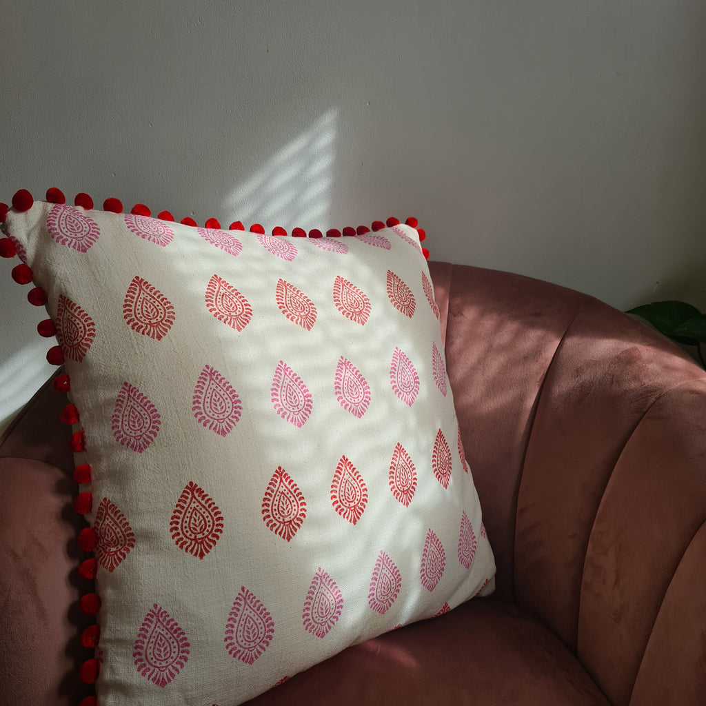 Decorative pillow with red patterns and pom-pom trim on a neutral background
