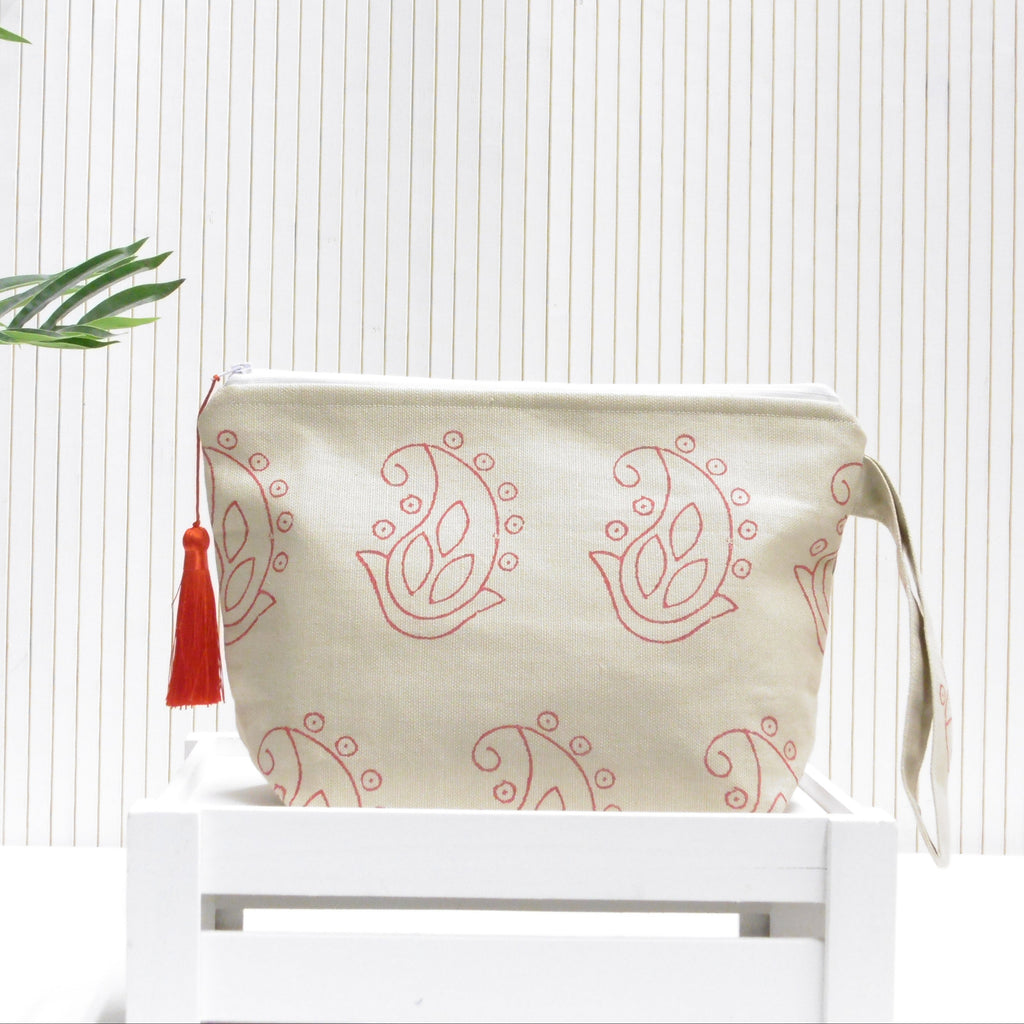 Beige pouch with pink paisley pattern and red tassel on a white surface with a light wooden background